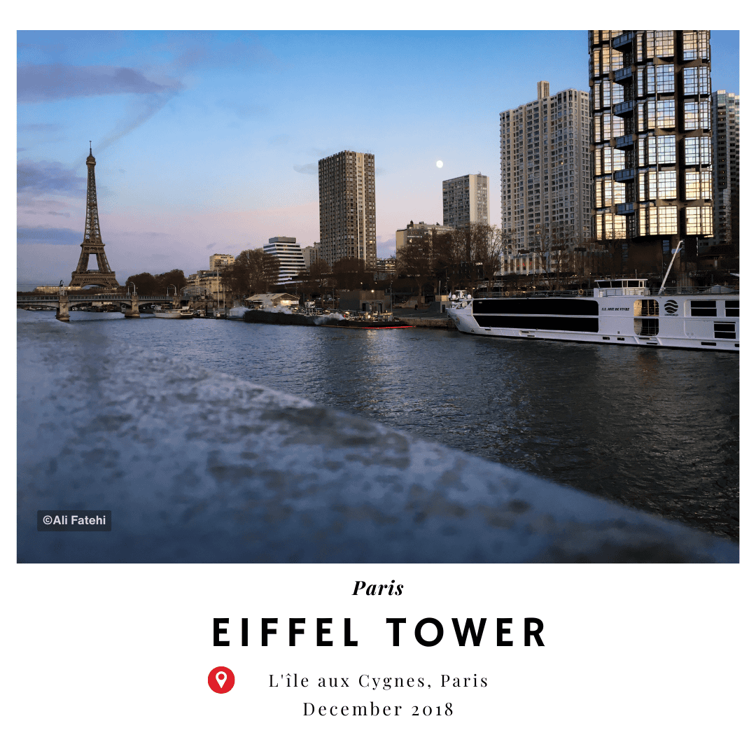 A view of the Eiffel Tower from L'île aux Cygnes in Paris, with a boat on the Seine River and buildings in the background, taken in December 2018.